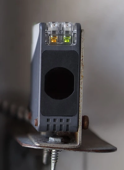 Professional garage door technician adjusting and aligning photo-eye safety sensors at garage door base, showing expert sensor repair work including wiring inspection, beam alignment, and safety system calibration to prevent random reversals for Louisville homeowners