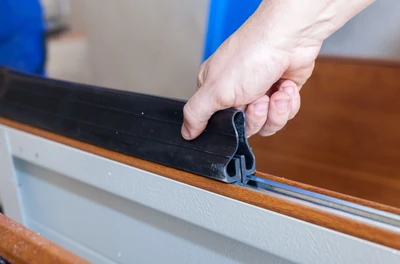 Professional garage door technician installing new bottom weather seal and perimeter rubber weatherstripping, showing expert seal replacement service to prevent drafts, water infiltration, pest entry, and improve energy efficiency for Louisville residential properties